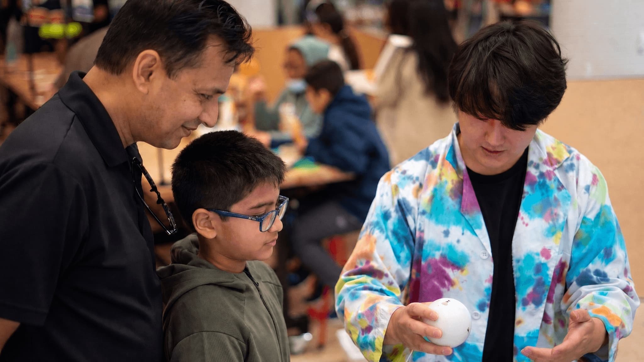 A Qolour educator showing a Qubi to a curious kid and his dad