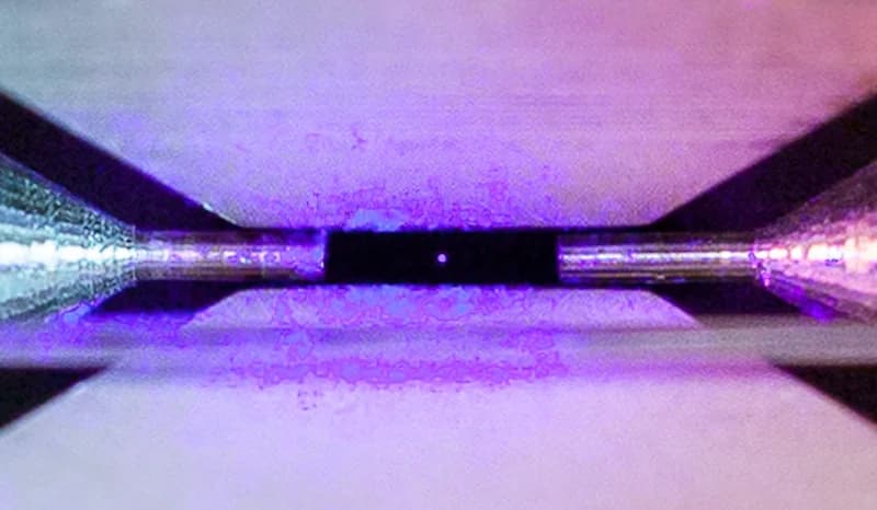 A single strontium ion suspended between two electrodes in an ion trap, glowing under laser light