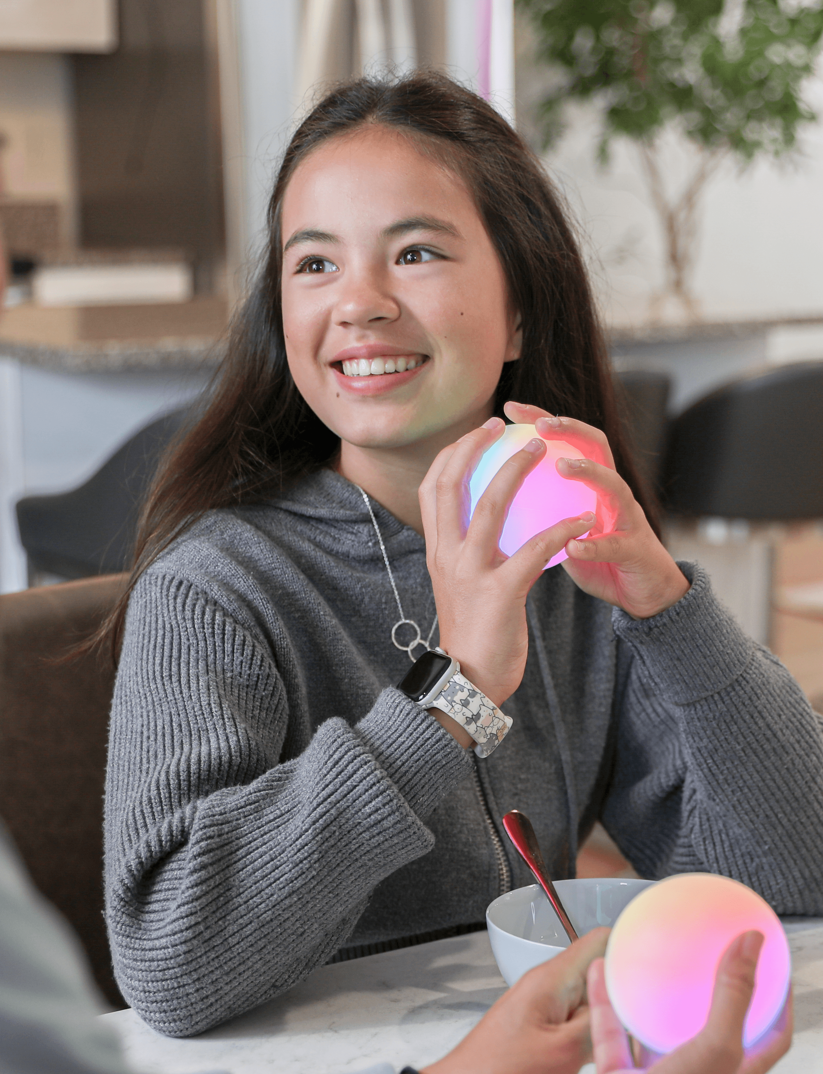A smiling teenager holding a glowing Qubi at the breakfast table